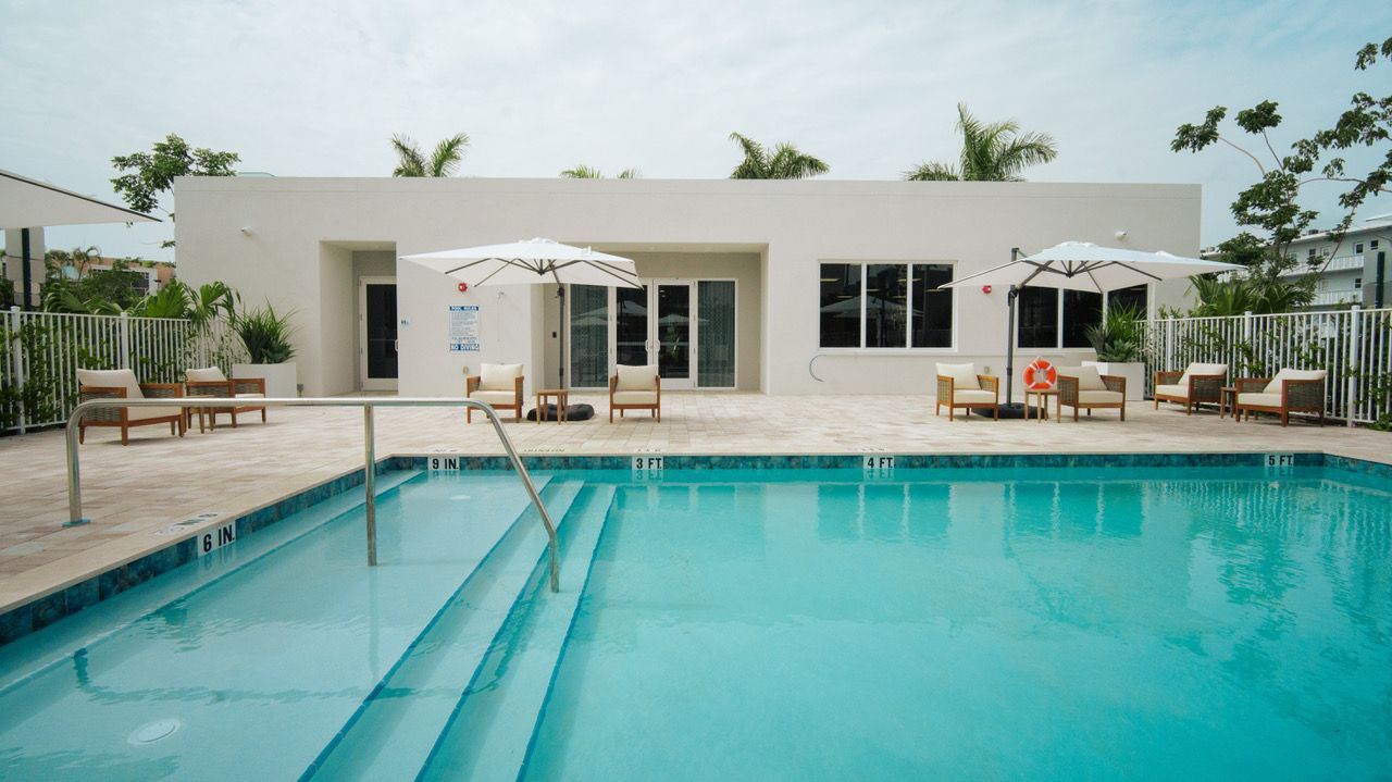 Modern white villa with a turquoise swimming pool and lounge chairs under a cloudy sky at Atlantica at Dania Beach apartments in Dania Beach, FL.