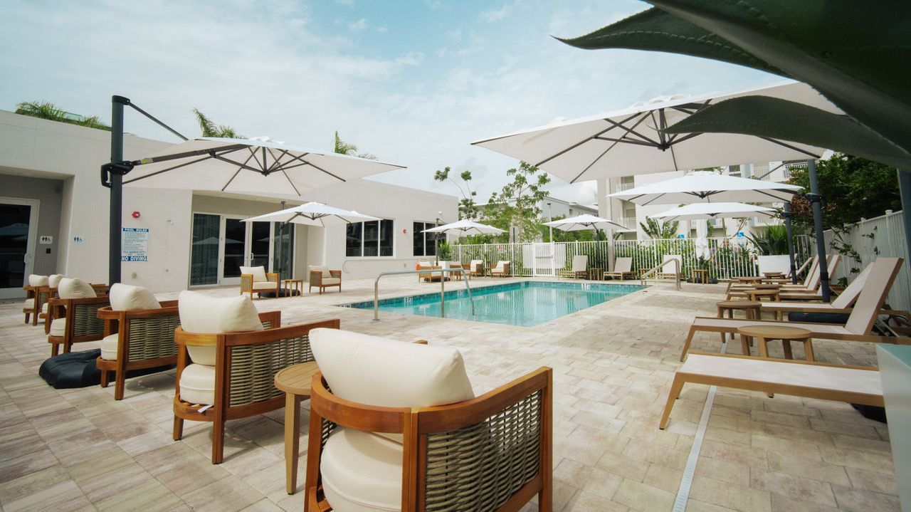 Luxury resort pool with white umbrellas, lounge chairs, and turquoise water under a bright sky at Atlantica at Dania Beach apartments in Dania Beach, FL.