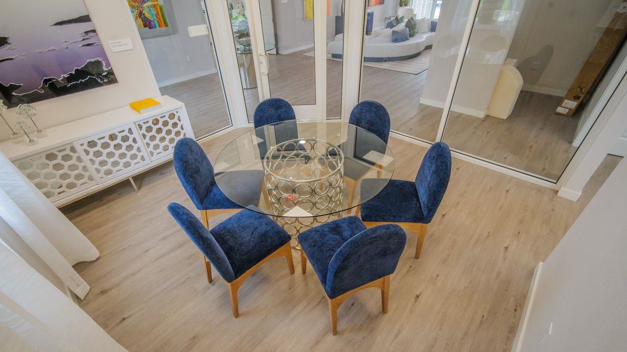 Glass dining table with six blue chairs in a bright modern room at Atlantica at Dania Beach apartments in Dania Beach, FL.