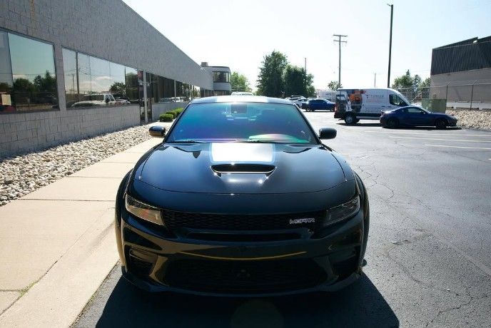 Black sports car parked on a sunny lot, front view with two cars in the background