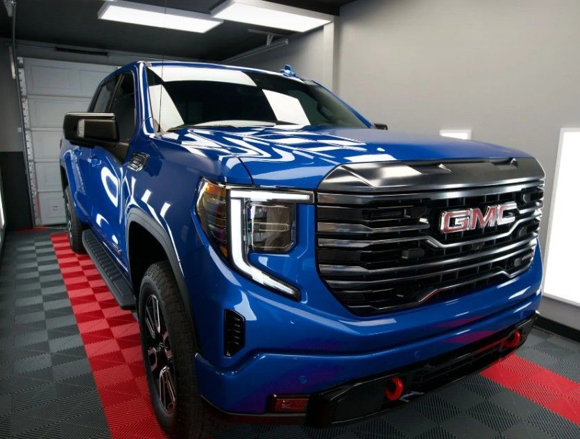 Blue GMC pickup truck parked indoors on a red-and-black checkered floor under bright lights
