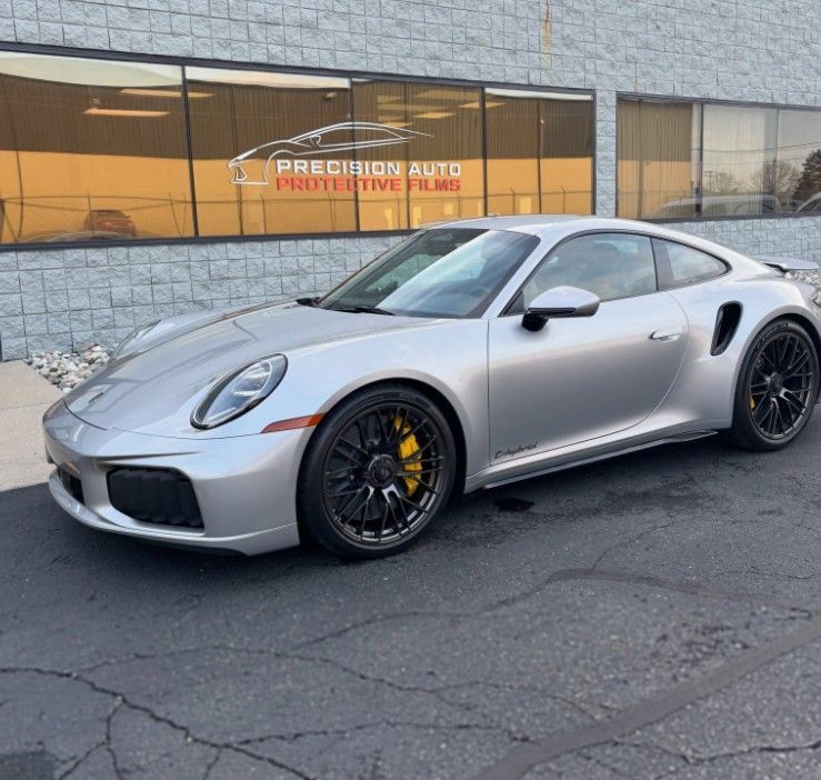 Silver Porsche 911 parked outside a storefront with black wheels and yellow brake calipers