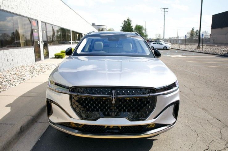Front view of a silver Lincoln SUV parked on a sunny street beside a modern building