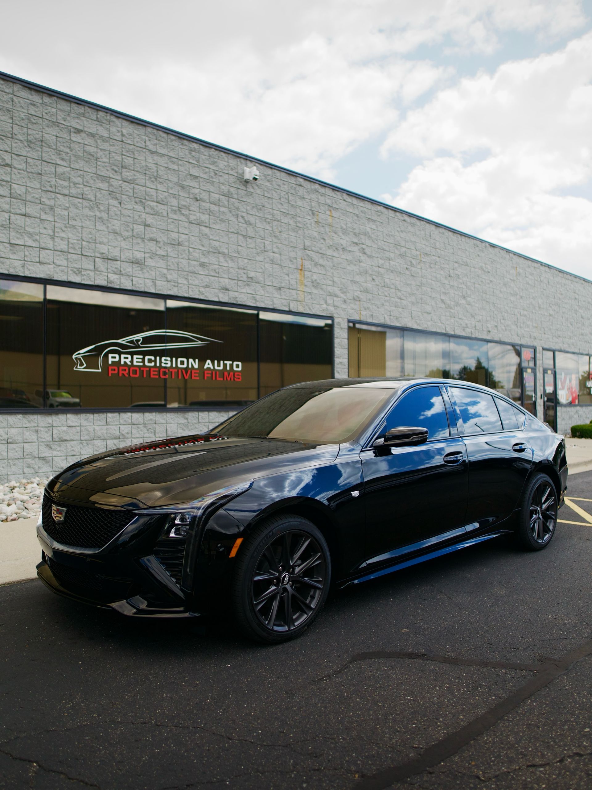 Black sports sedan parked outside a brick auto dealership on a wet lot