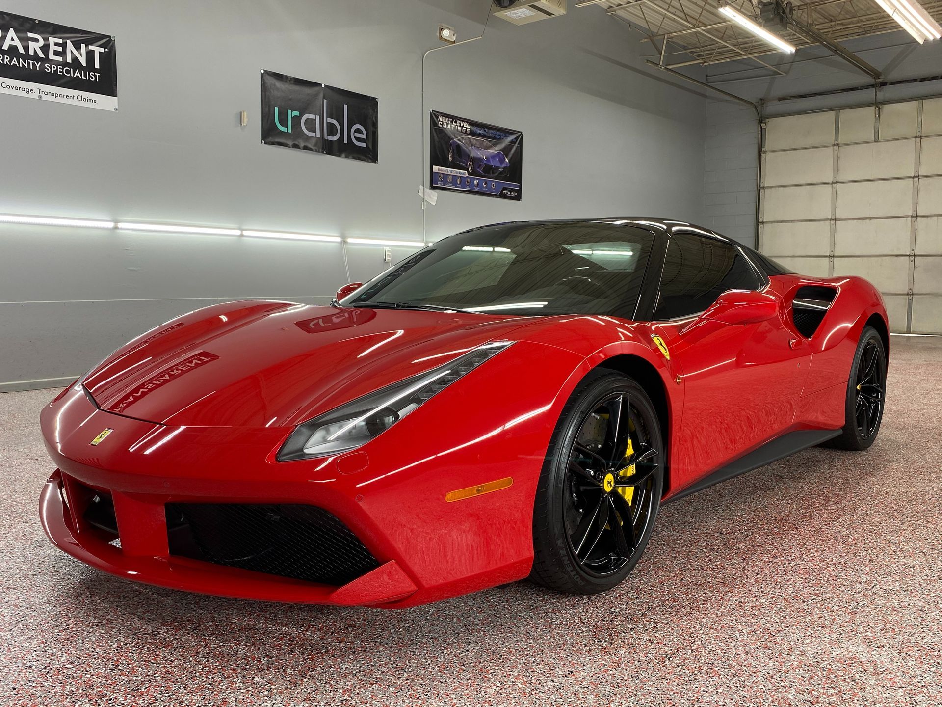 Red Ferrari sports car in a showroom, angled front view, with black wheels and yellow brake calipers.