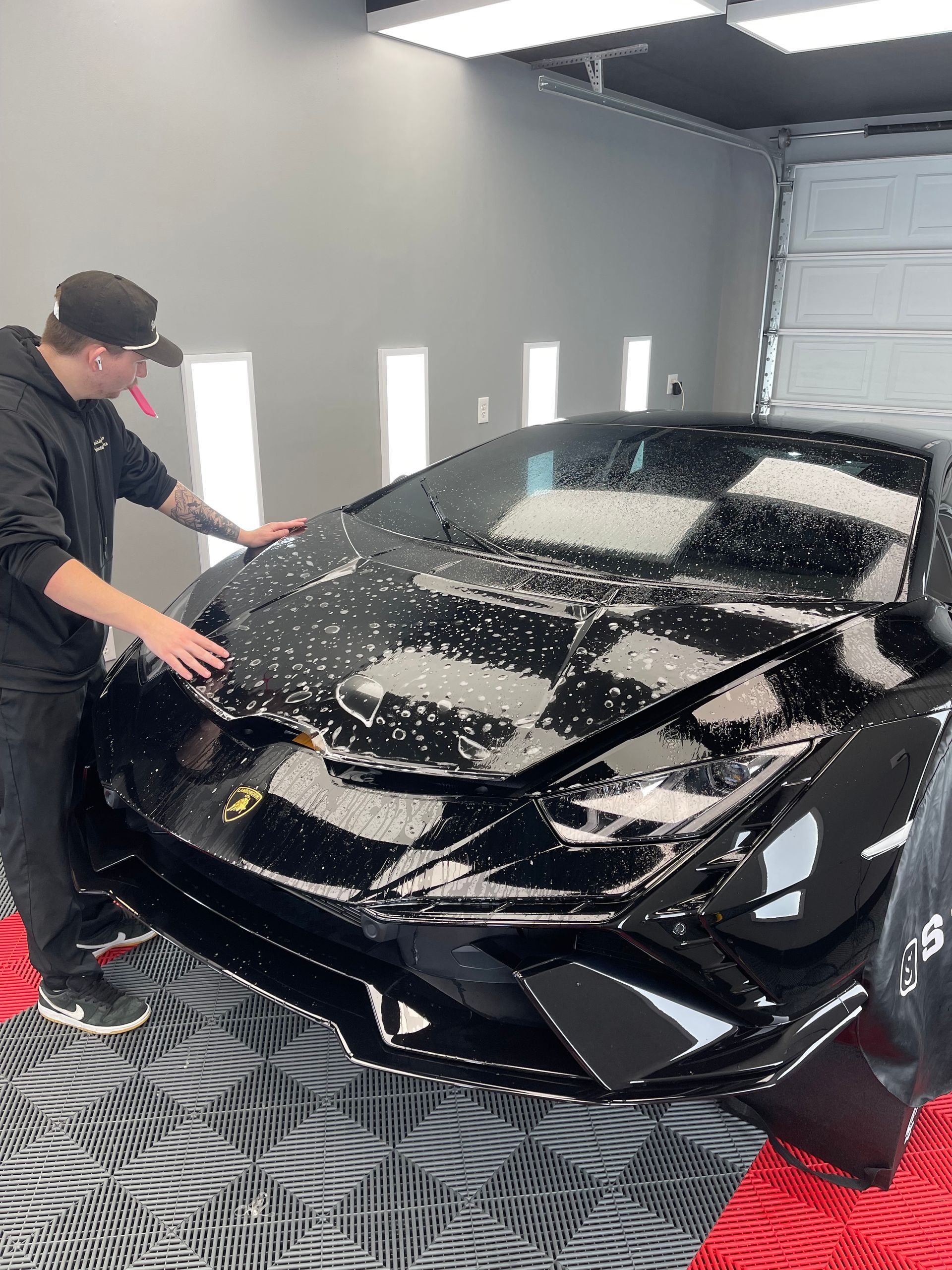 Gray Tesla car in a car bay with a red and black tiled floor and overhead lighting.