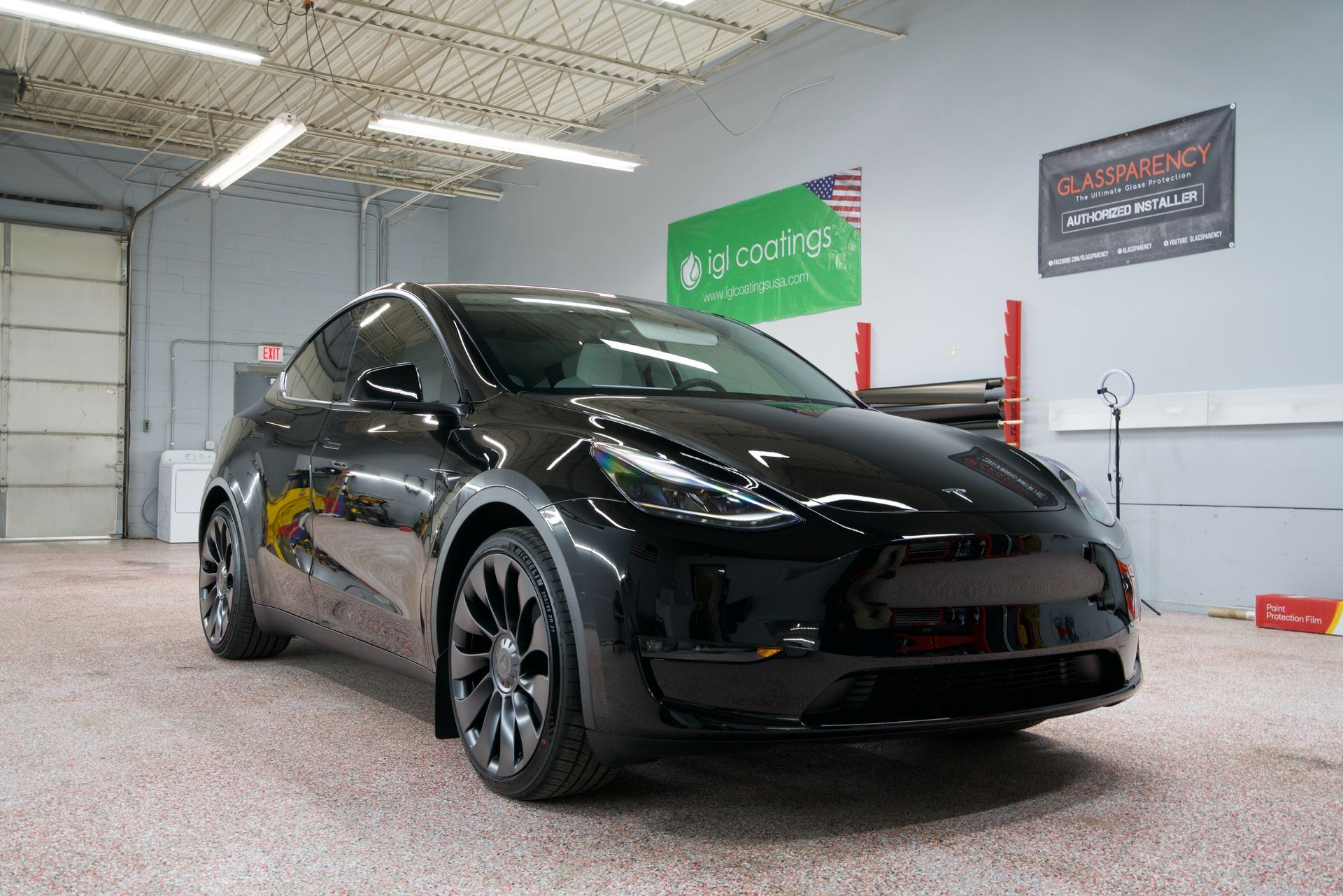 Black Tesla in a garage with red lift posts and wall signs