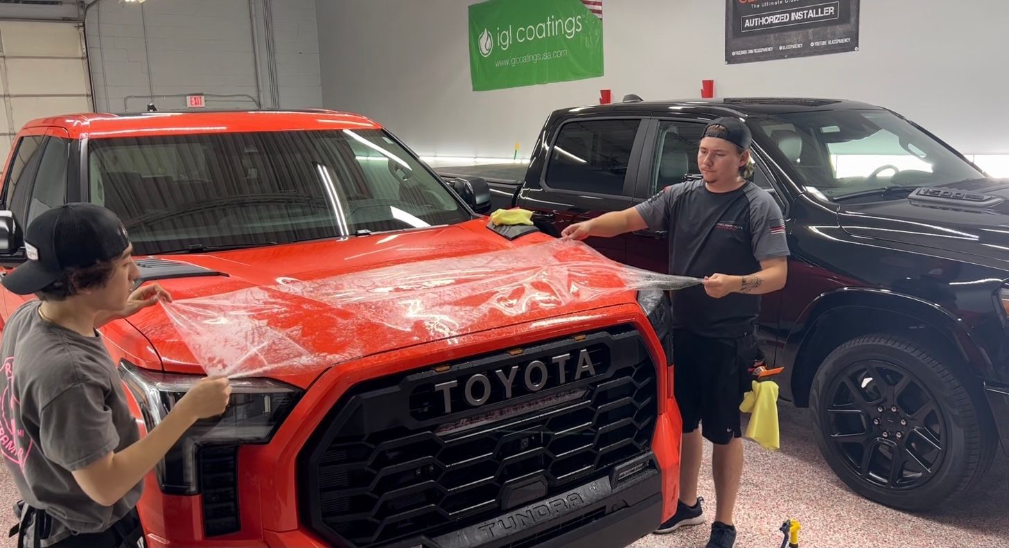 Two men are standing next to a red toyota truck in a garage.