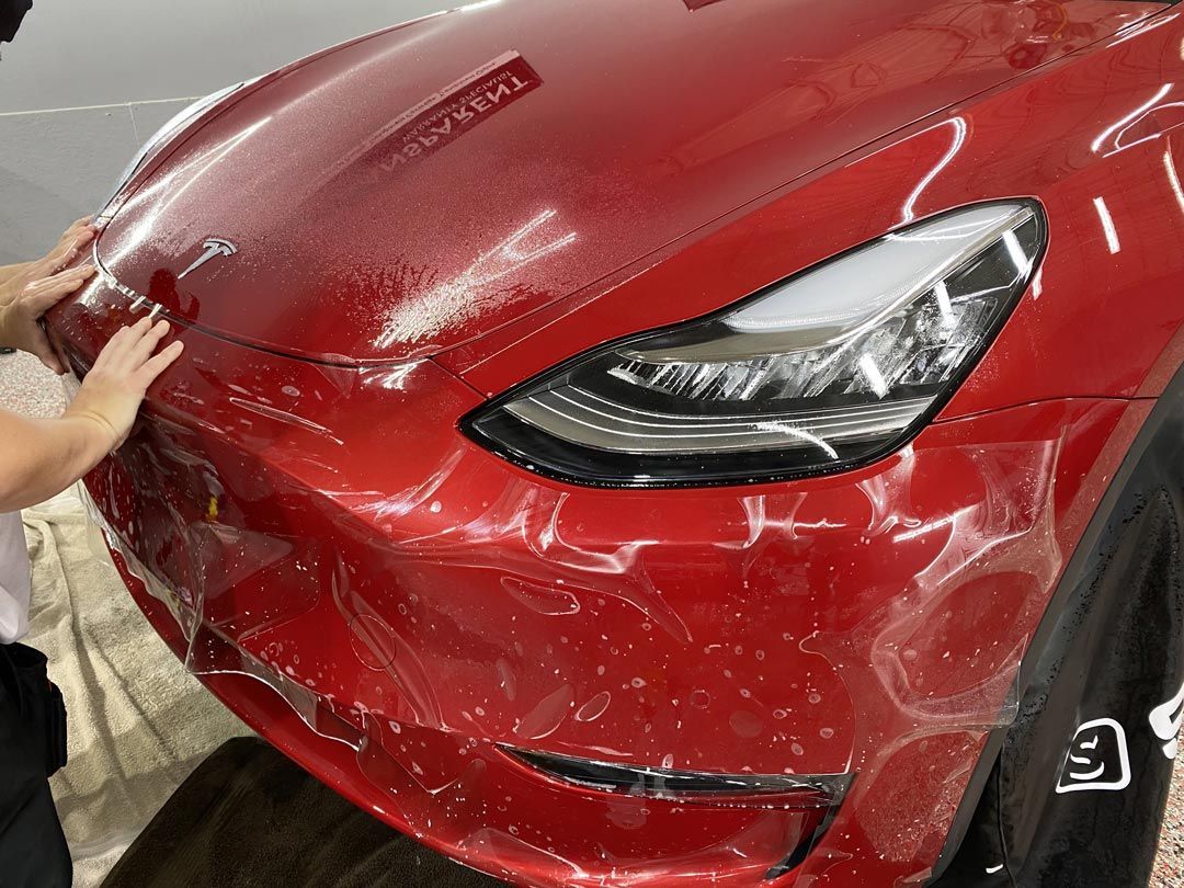 A person is covering the front of a red tesla model y with plastic wrap.