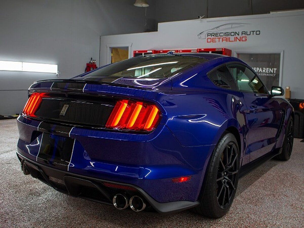 Blue Ford Mustang Shelby parked inside a garage. It has black stripes and black rims.