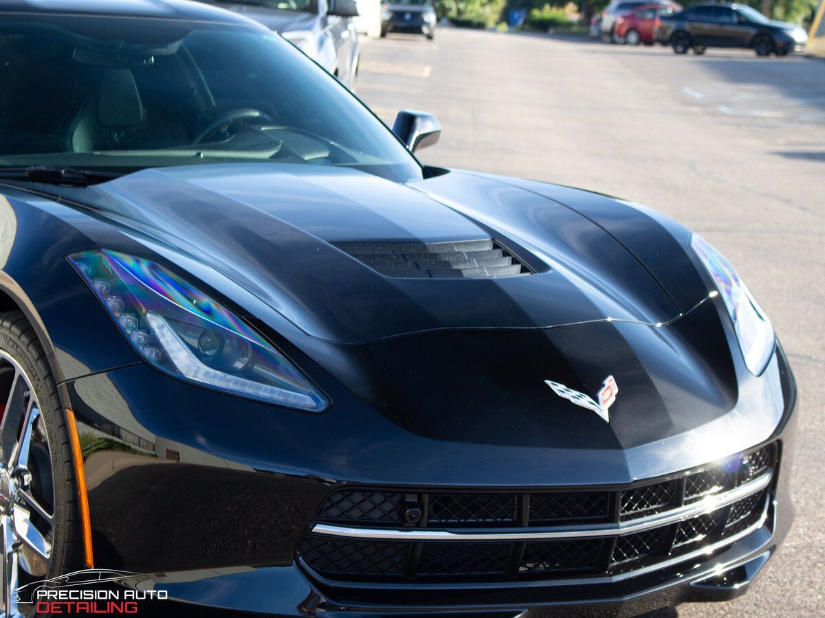 Black Corvette sports car with racing stripes, shiny finish, parked outdoors.