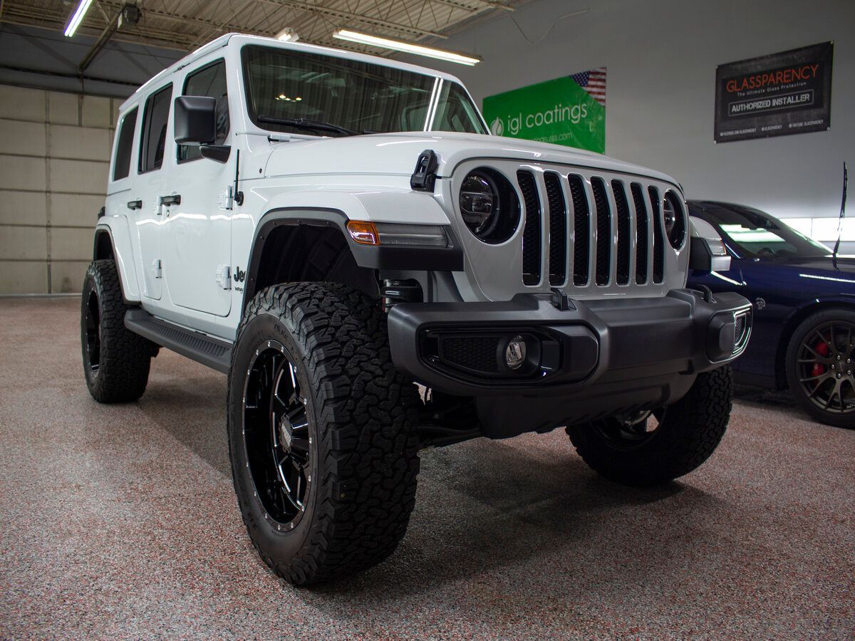 White Jeep Wrangler with black accents on display at a car dealership.