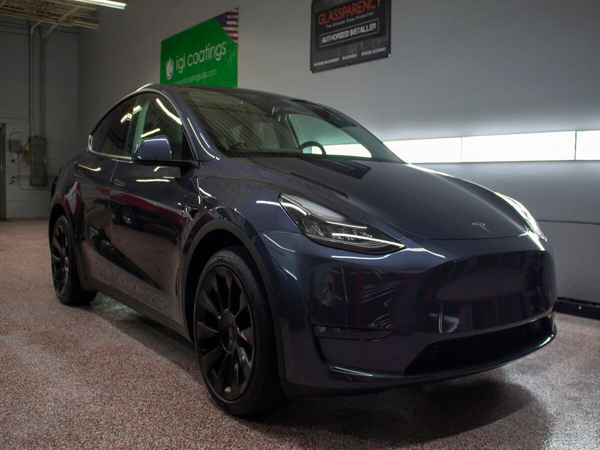 Dark blue Tesla Model Y SUV parked in a garage with a glossy floor.