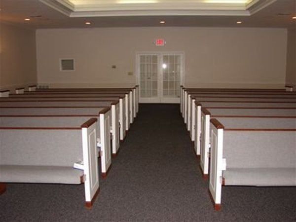 Empty chapel interior with rows of pews facing double doors.
