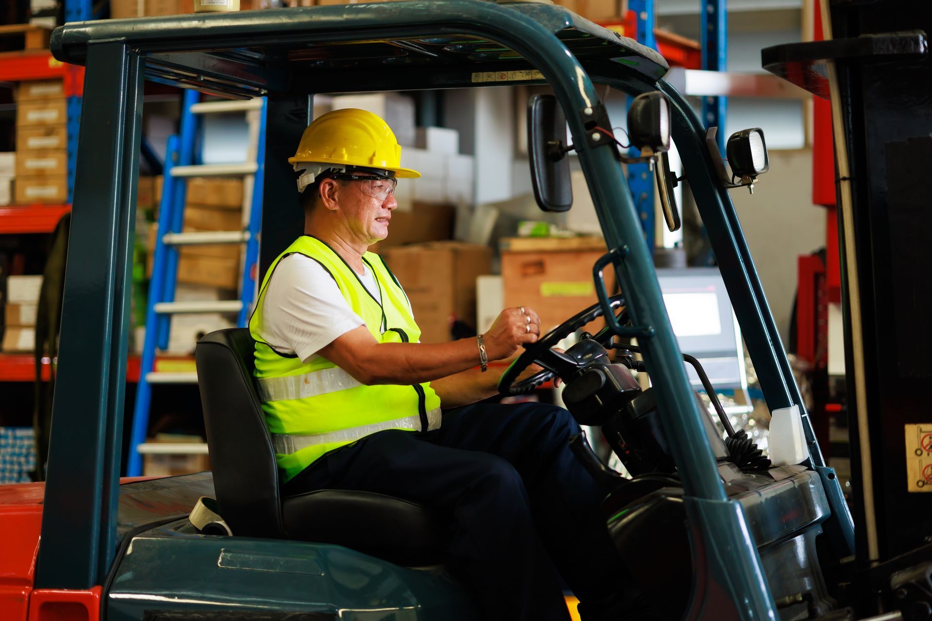 A person in a hard hat and high-visibility vest operating a forklift in a warehouse.