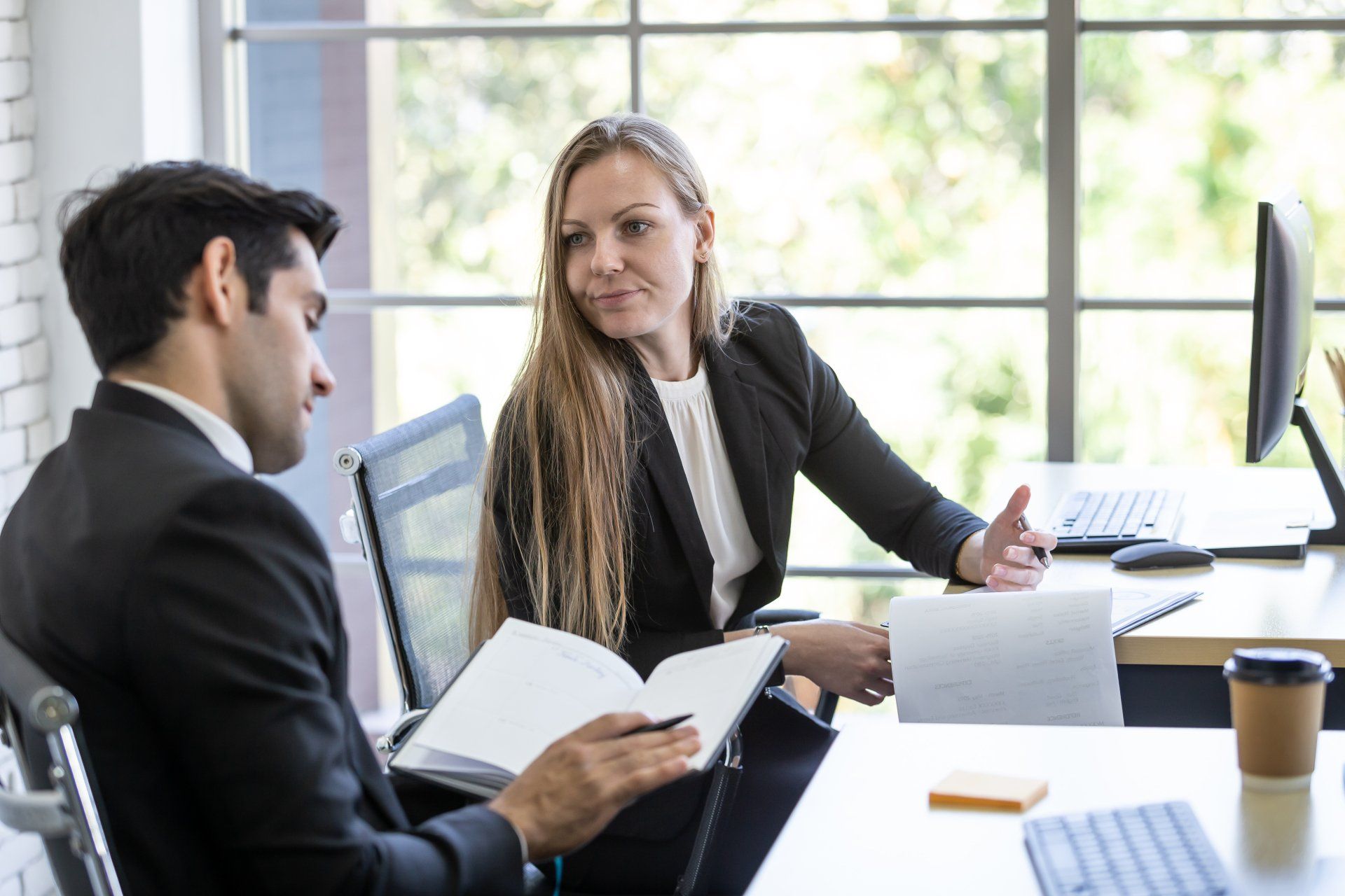 A man and a woman are sitting at a desk in an office having a conversation.
