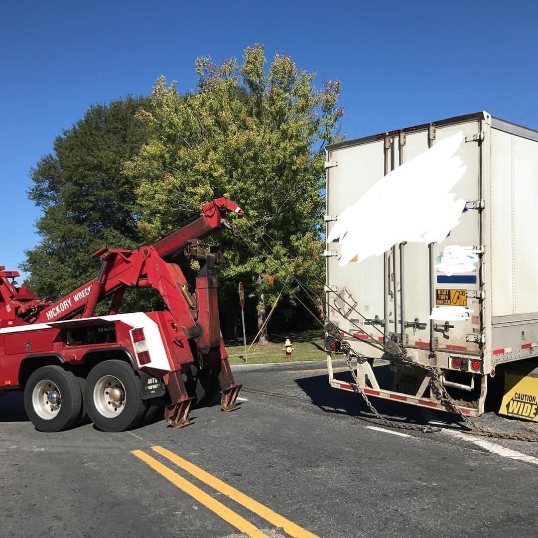 A red tow truck is towing a white semi truck