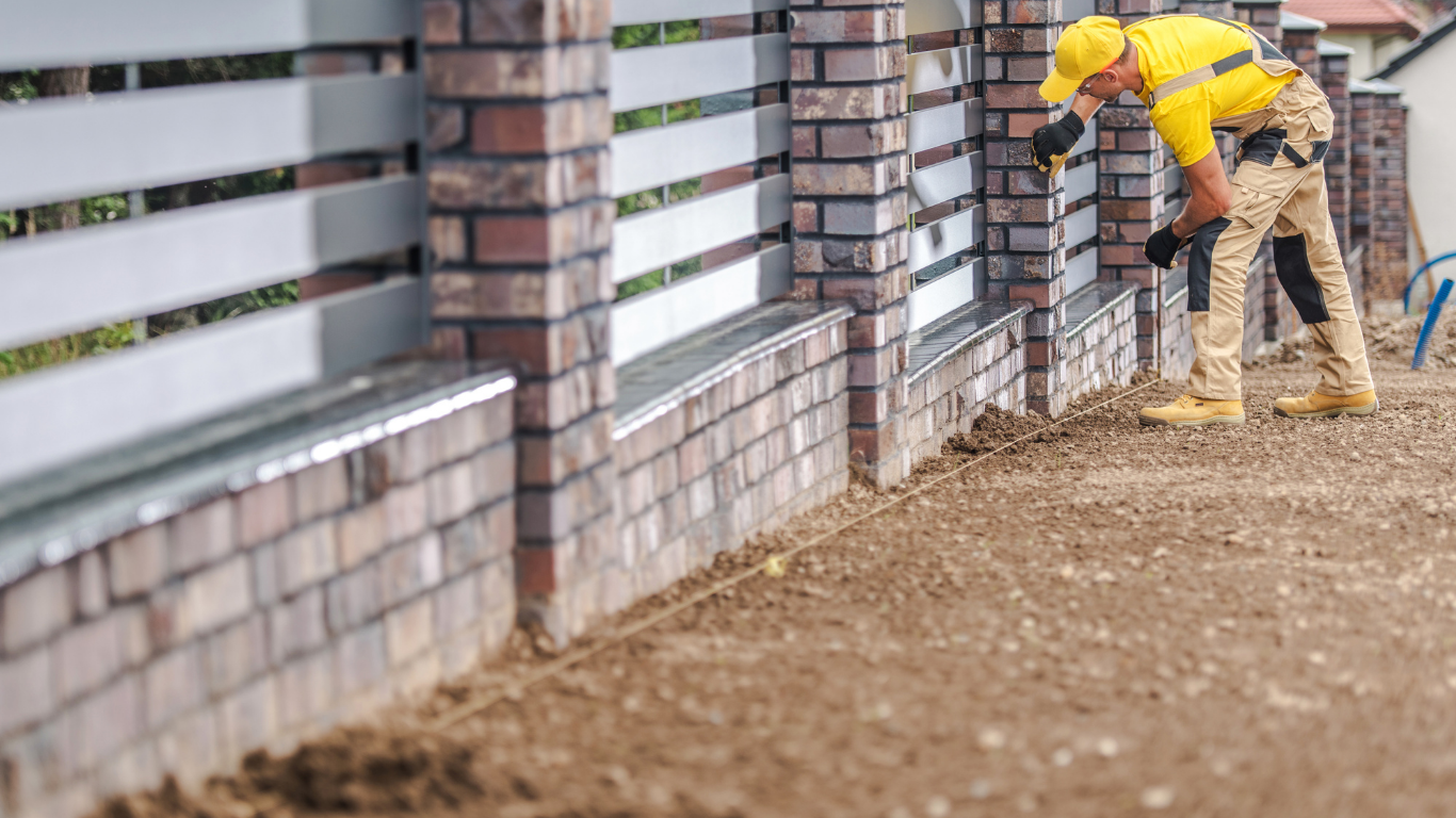 Worker in yellow jacket using a tool beside a brick wall at a construction site