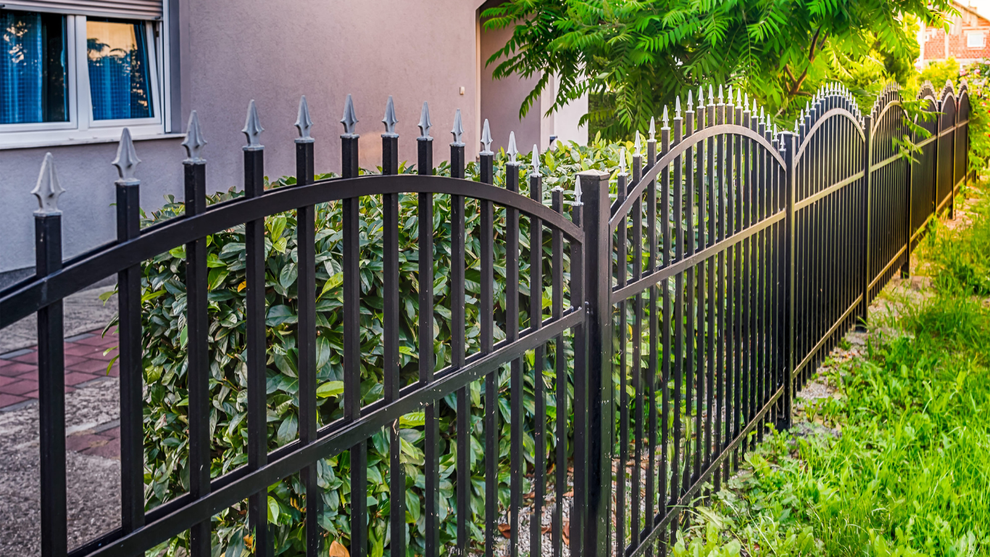 Black metal fence along a green yard beside a house and sidewalk.