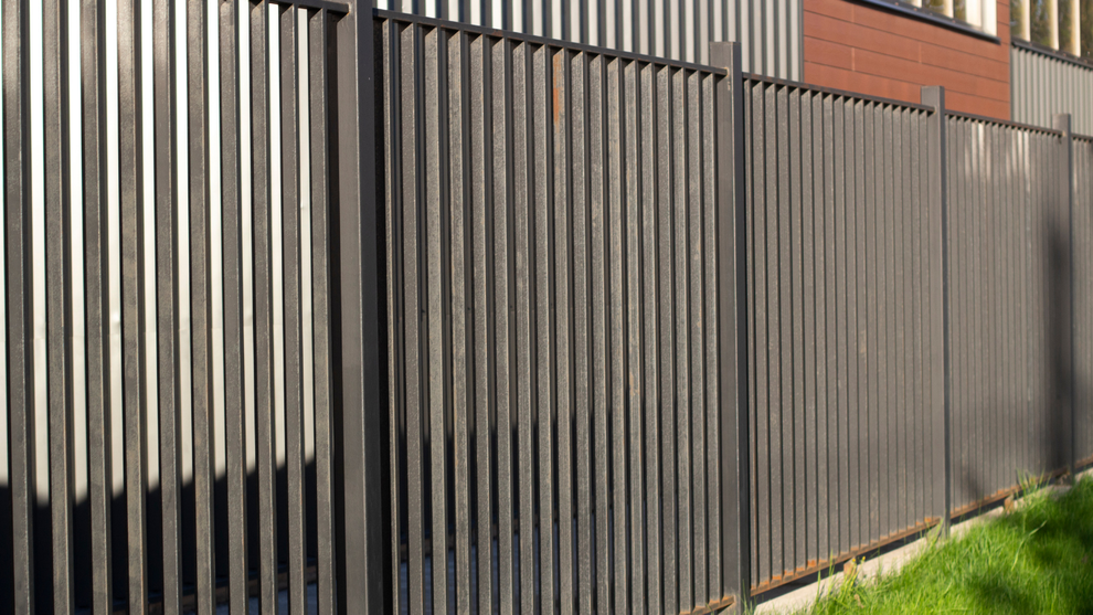 Tall black metal fence with vertical slats beside grass and a brick building