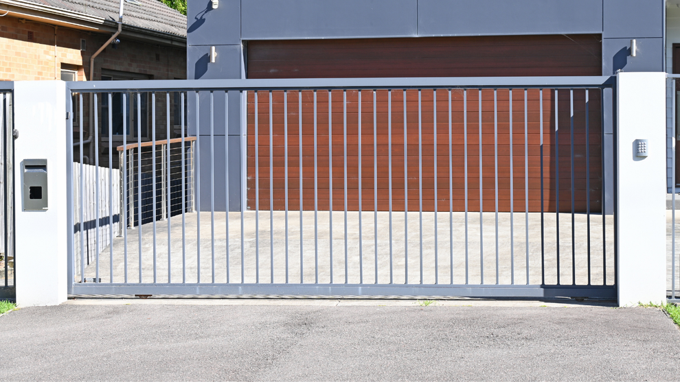 Gray metal sliding gate in front of a modern house and garage