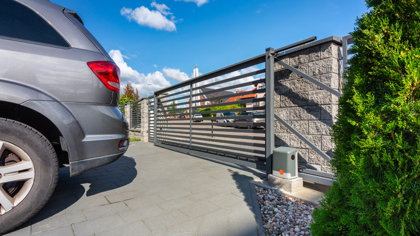 Silver SUV beside a modern sliding metal gate along a residential driveway under a blue sky