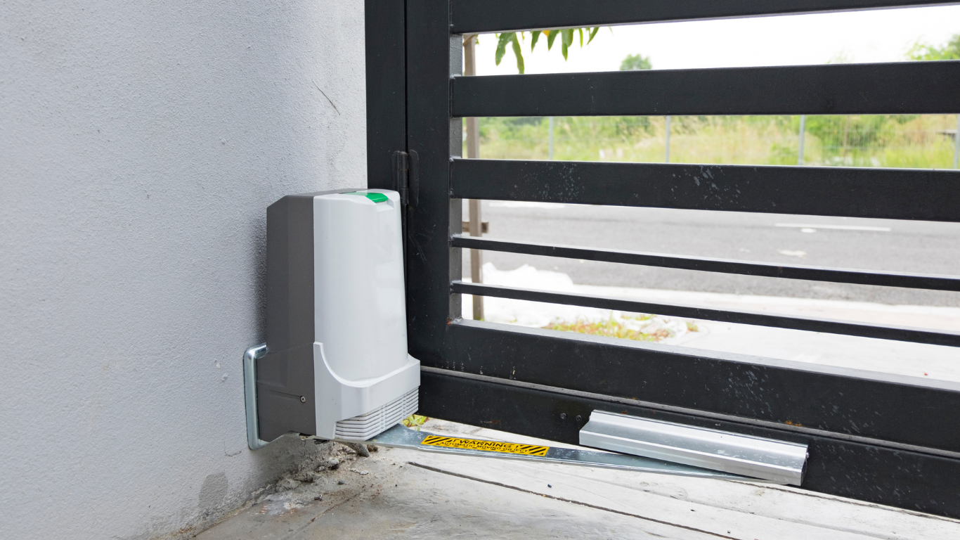 Small gray device mounted beside a black gate on a concrete floor indoors.