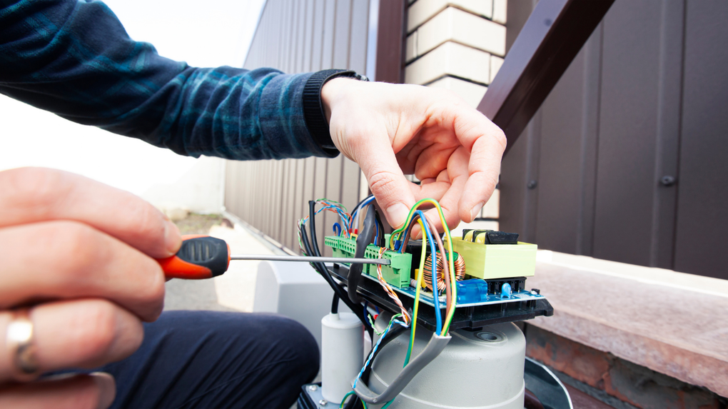 Person wiring a small outdoor electronics device with tools near a house wall.