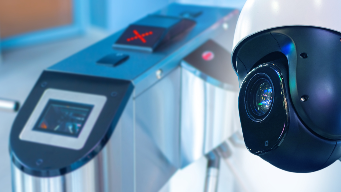 Security robot with camera lens beside a metallic kiosk with glowing red display in a modern facility