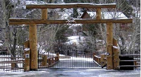 Snowy wooden gate at a park entrance with a closed metal fence and bare winter trees