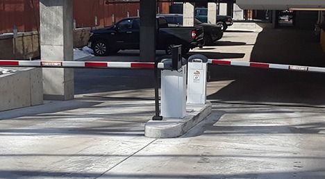 Parking barrier arm across driveway at a gated entrance with parked cars in the background