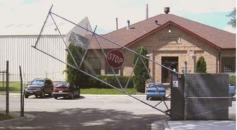 Broken gate across driveway in front of a building, with stop sign and parked cars behind it.