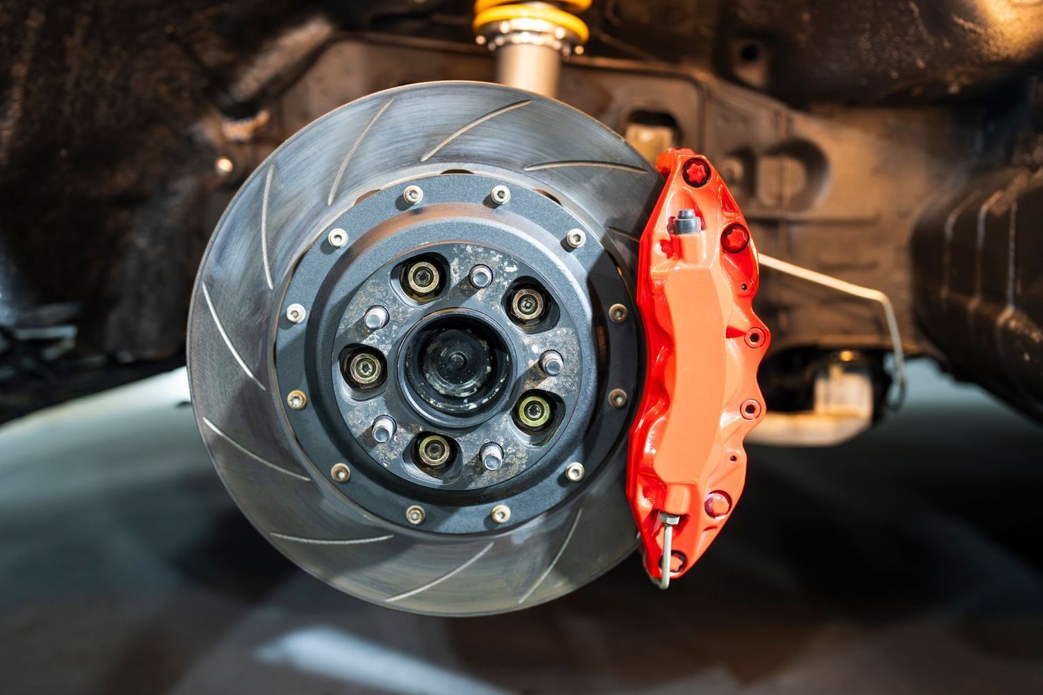 Close-up of a slotted automotive brake rotor and a vibrant red brake caliper mounted on a vehicle wheel hub.