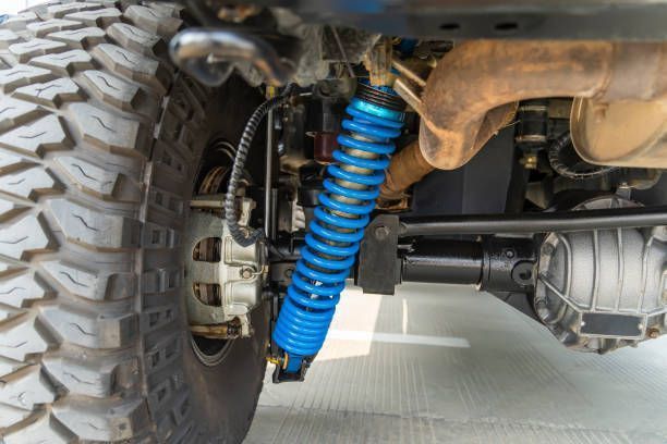 A close-up of a blue coil-over shock absorber on a vehicle's undercarriage next to a rugged off-road tire.