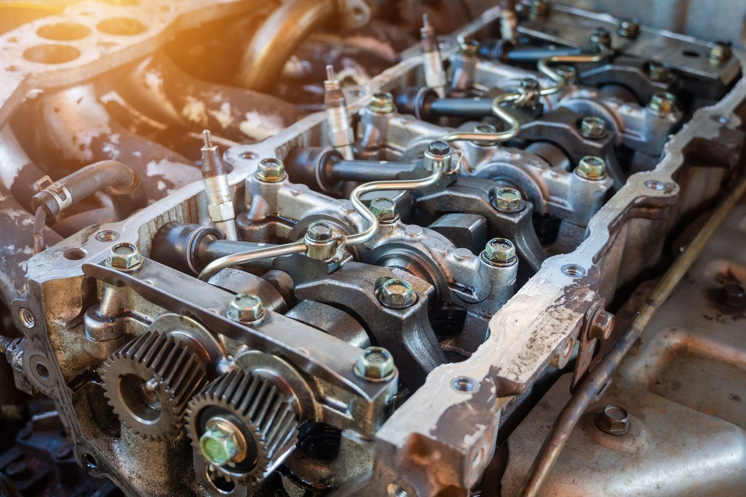 Close-up of a disassembled car engine head showing exposed metallic gears, valves, and components in a workshop.