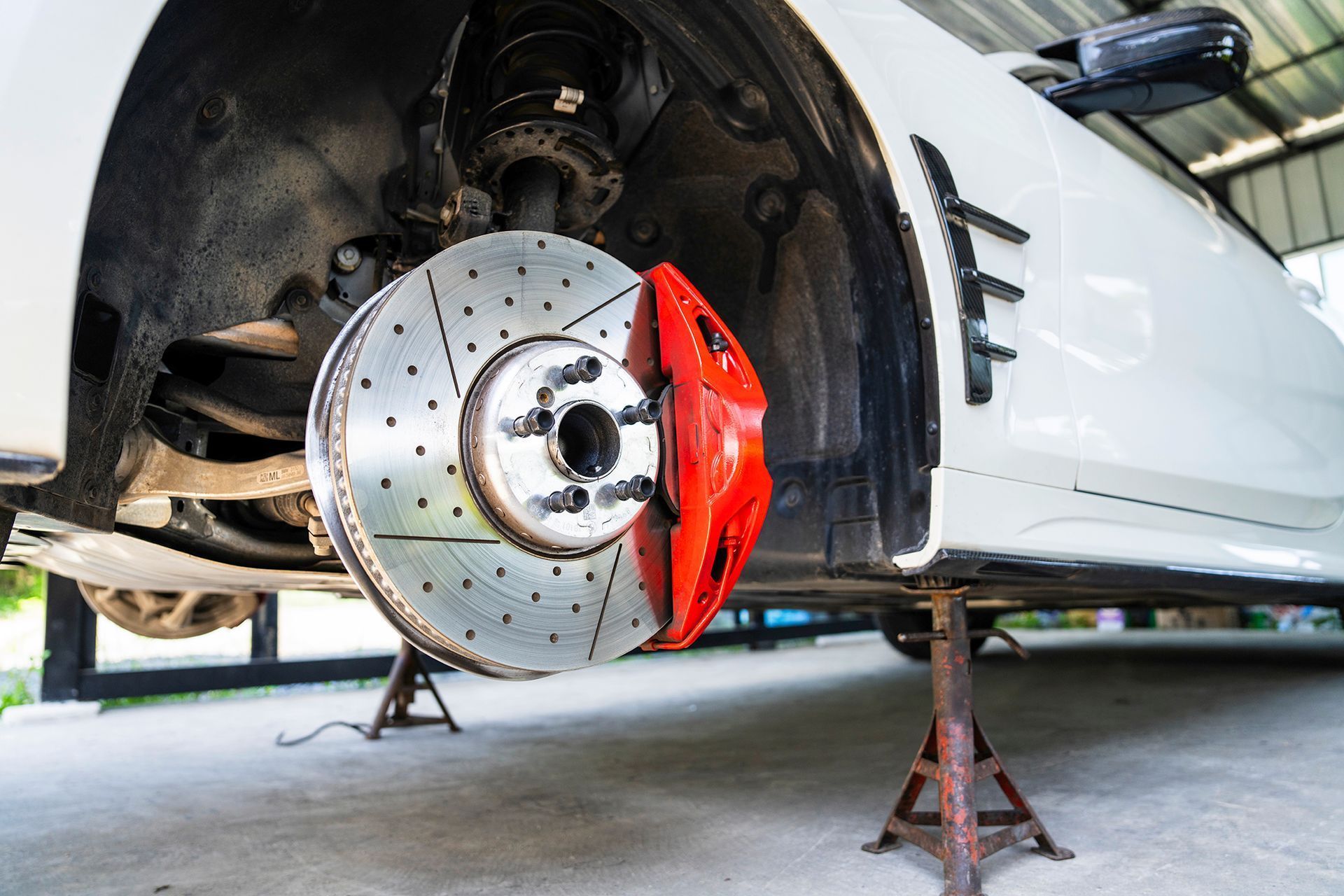 A car elevated on jack stands with its front wheel removed, showing the brake rotor and red brake caliper.