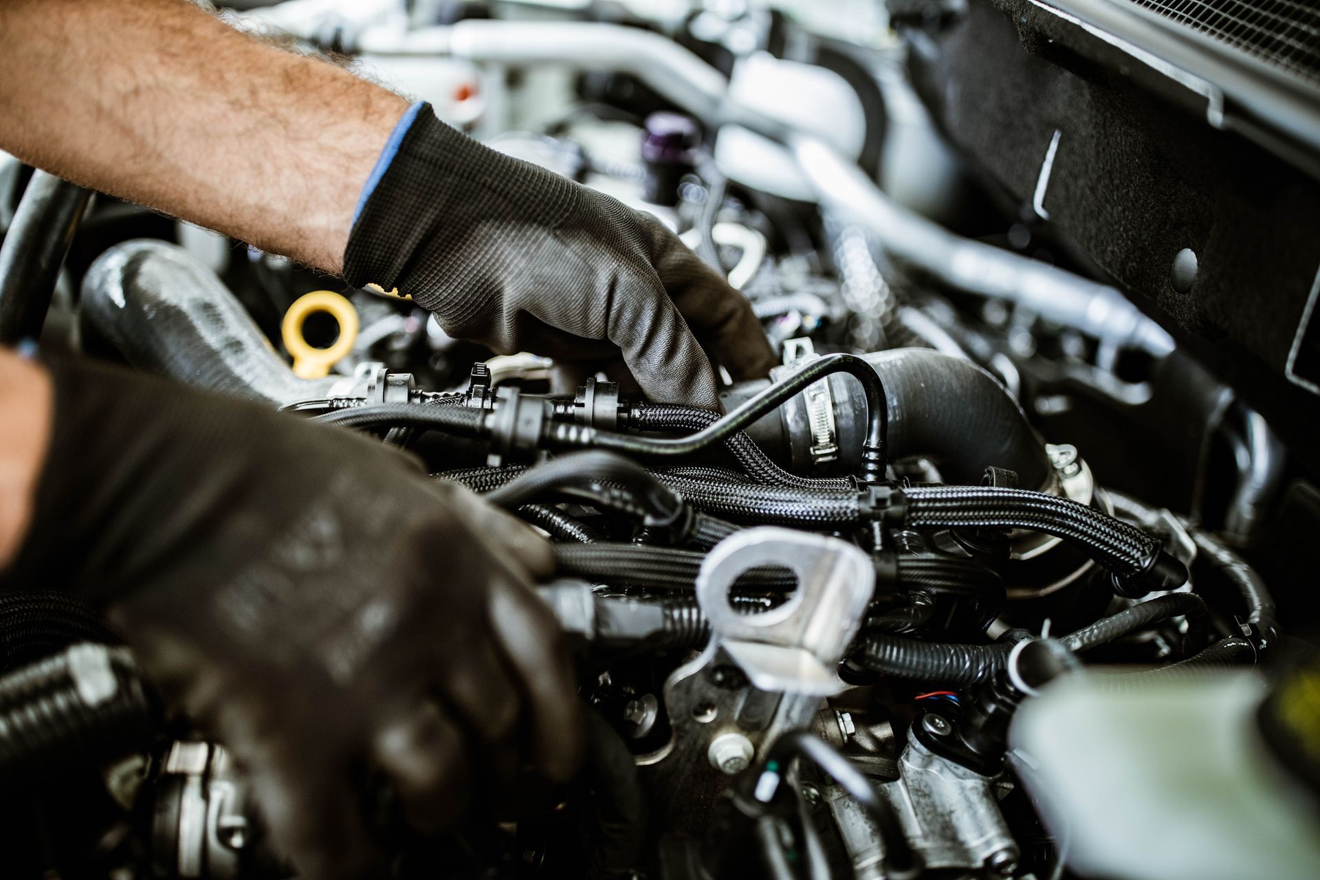 Mechanic wearing black gloves works on a complex car engine.