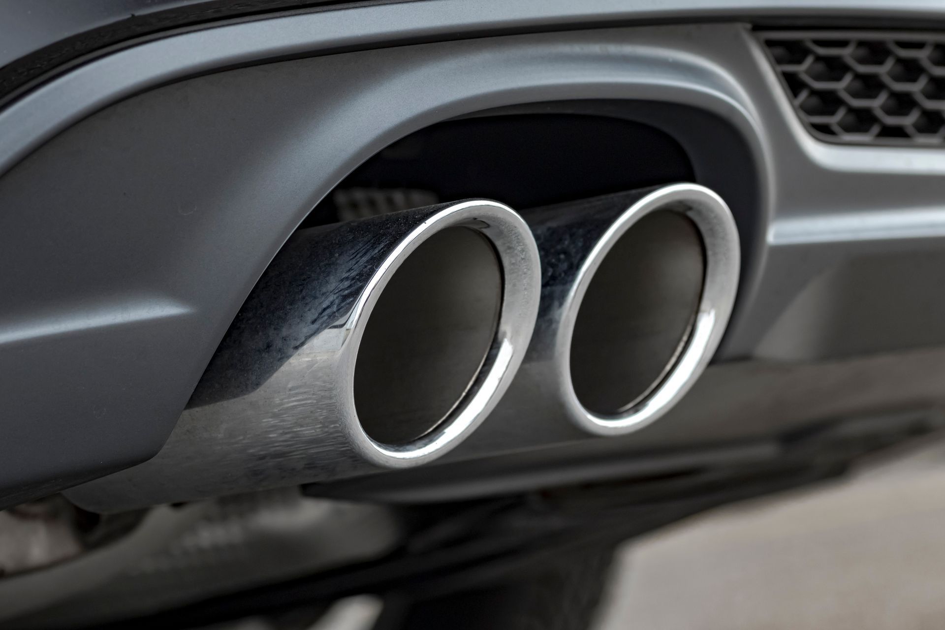 A close-up of a vehicle's dual chrome exhaust pipes integrated into a dark gray bumper.