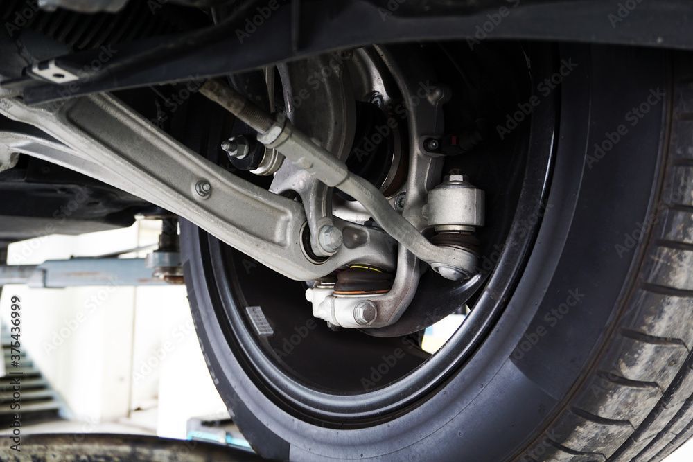 Close-up view of the mechanical suspension components, control arm, and tie rod of a car wheel raised on a vehicle lift.