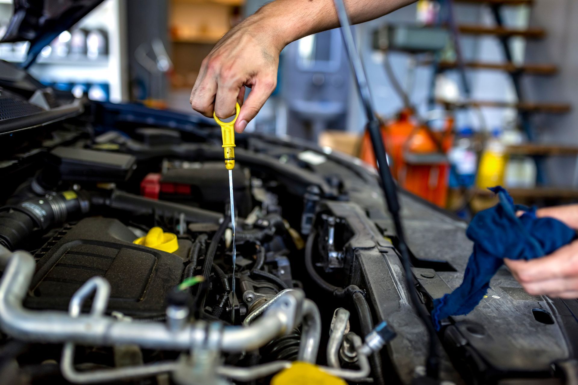 A mechanic checks the oil level in a car engine using a dipstick, holding a blue cloth in their other hand.