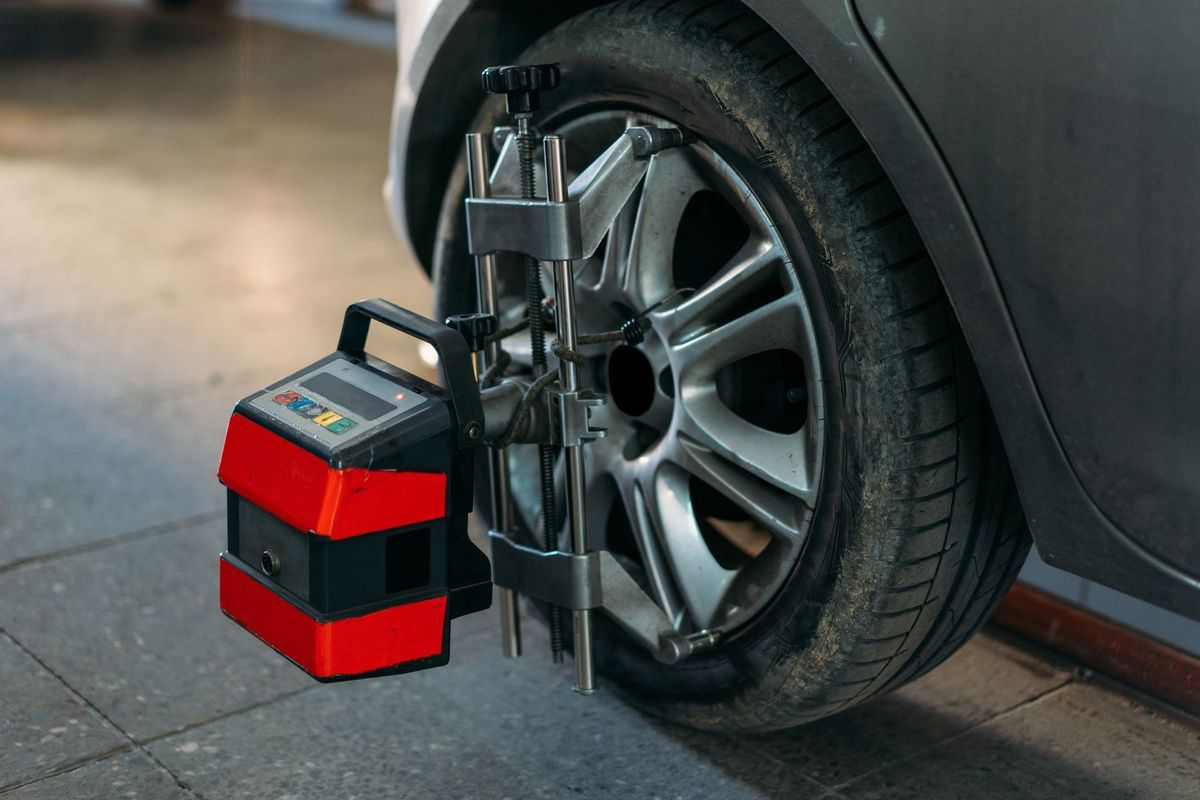 A car tire in a garage with a red and black wheel alignment sensor mounted to the rim.
