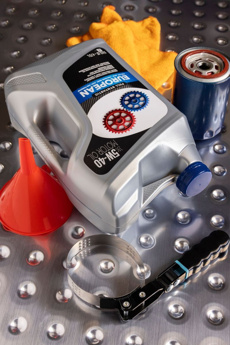 A container of 5W-40 motor oil, an oil filter, an orange funnel, and an oil filter wrench on a metal diamond-plate surface.