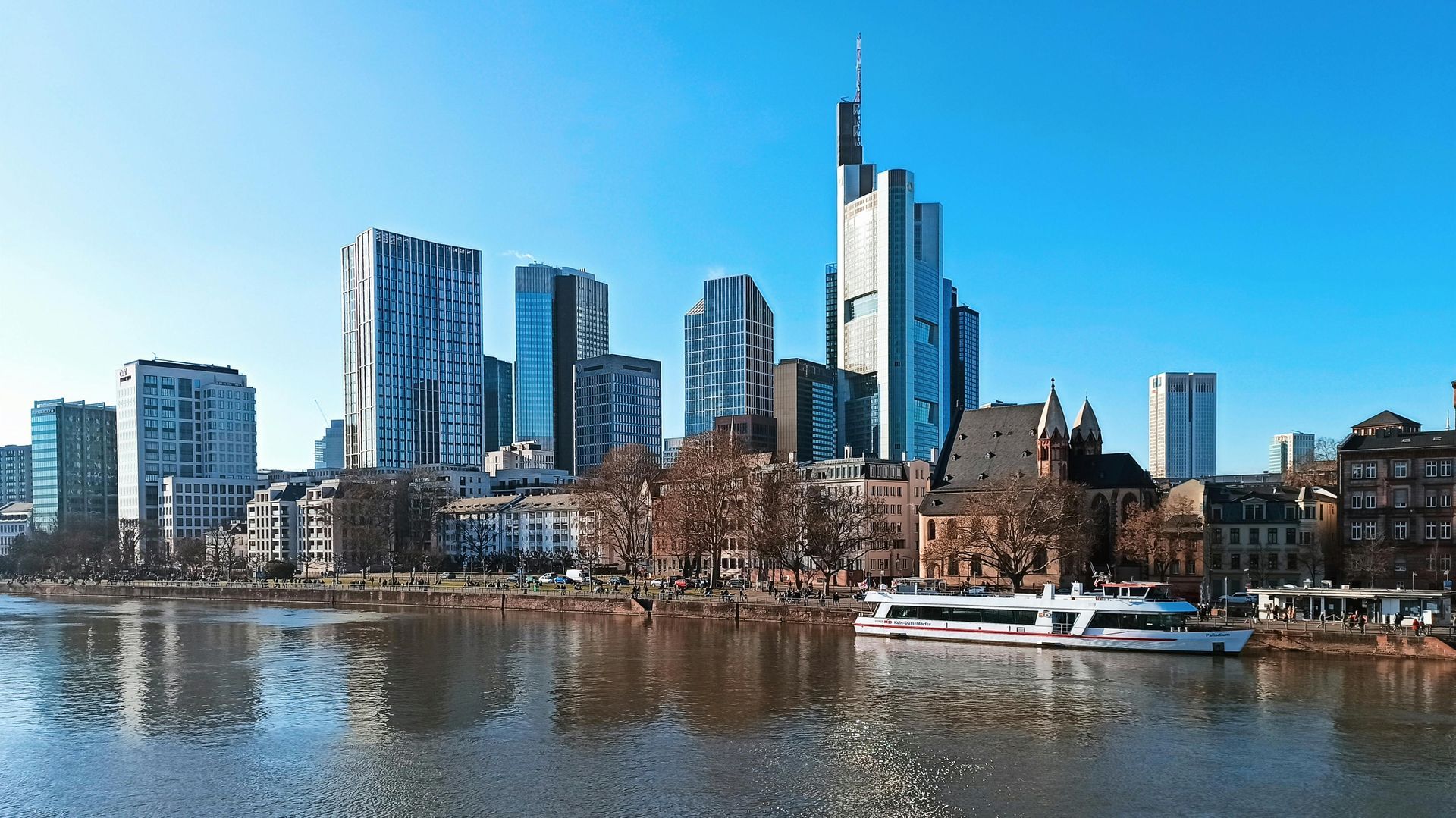 Stadtsilhouette auf der anderen Flussseite unter klarem, blauem Himmel, im Vordergrund Boote.