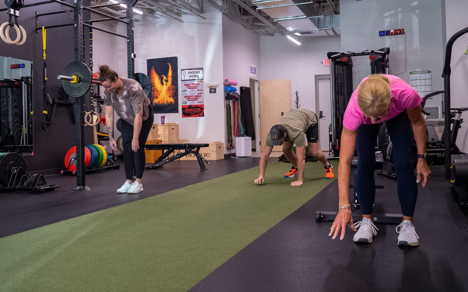 People in gym doing ab exercises, some with weights. Green turf, black equipment.