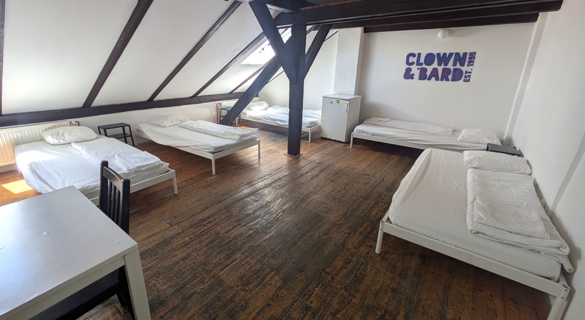 Attic room with several beds, a table, and a small refrigerator. A sign that reads