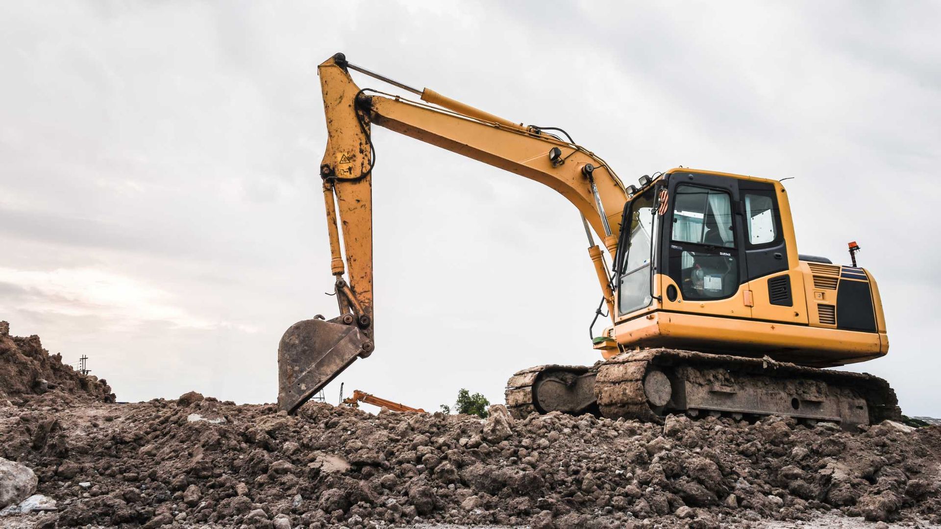 Yellow excavator digging through a rocky construction site under a cloudy sky