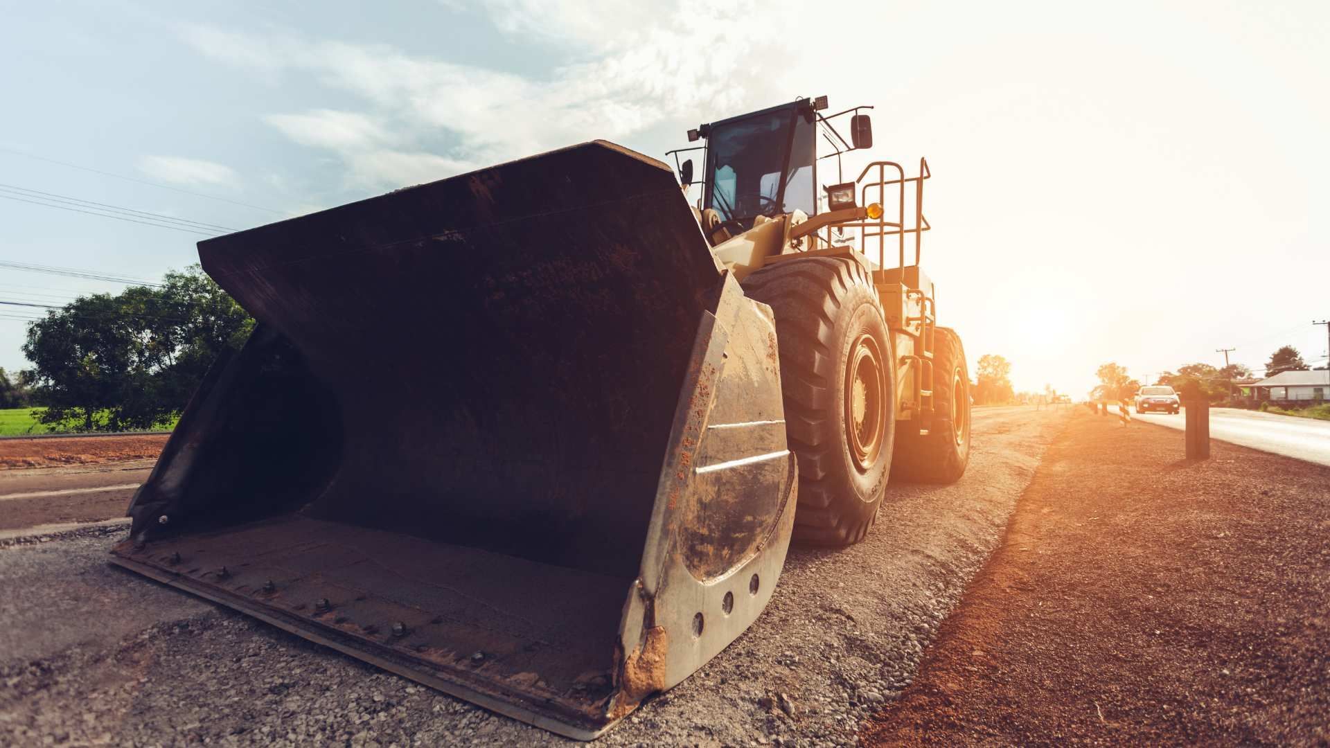 Bulldozer with raised bucket working on a road at sunset