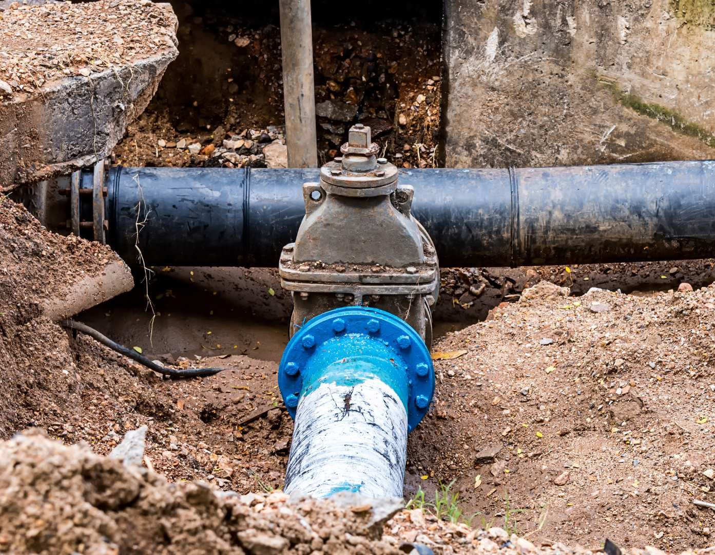 Exposed underground water pipe with blue and black joints in a dirt trench