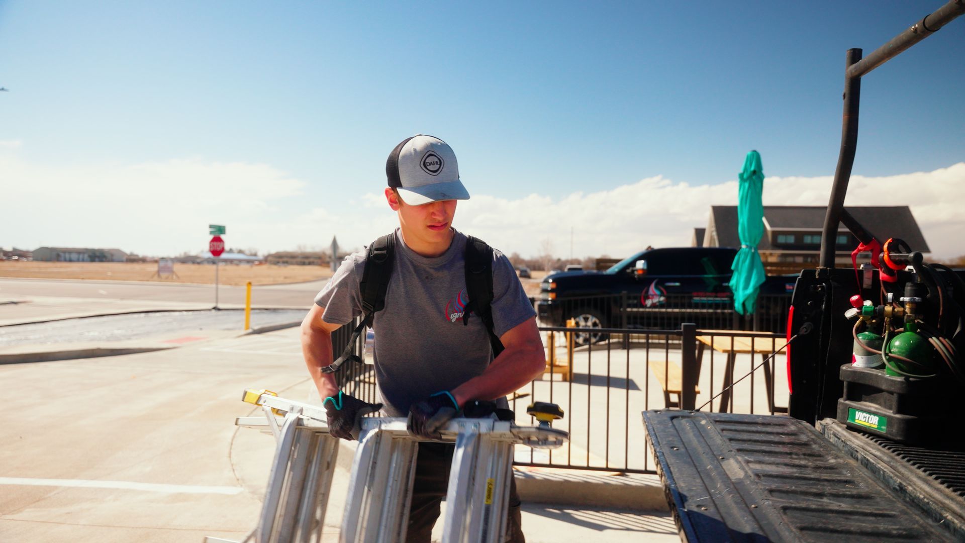 Person in a cap stands by metal barriers in a bright desert setting near a stage or event setup.