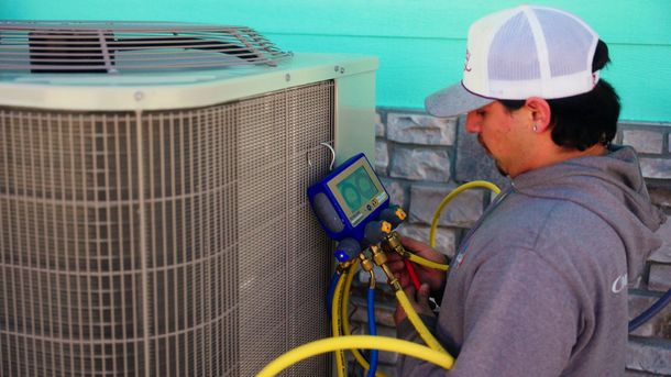 Technician servicing rooftop HVAC unit with gauges and hoses in a turquoise-walled setting